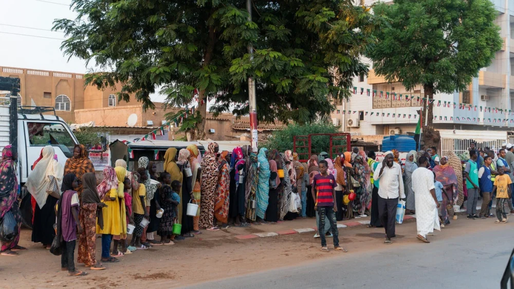 Familias desplazadas recientemente de El Fasher hacen fila en un reparto de alimentos, junto a residentes de larga duración, en Omdurman, la segunda mayor ciudad de Sudán. © ACNUR/Ala Kheir