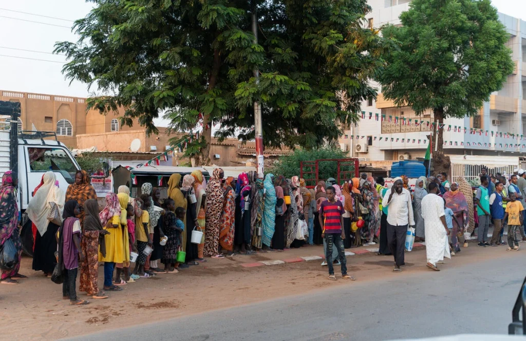 Familias desplazadas recientemente de El Fasher hacen fila en un reparto de alimentos, junto a residentes de larga duración, en Omdurman, la segunda mayor ciudad de Sudán. © ACNUR/Ala Kheir