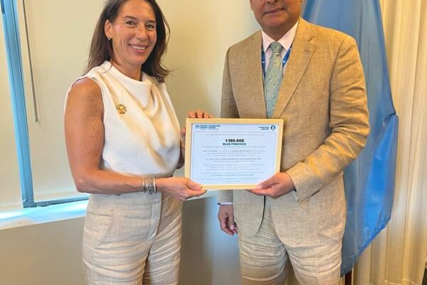 Two professionals stand side by side, smiling, as they hold a framed certificate together in a formal office setting with a blue flag in the background.