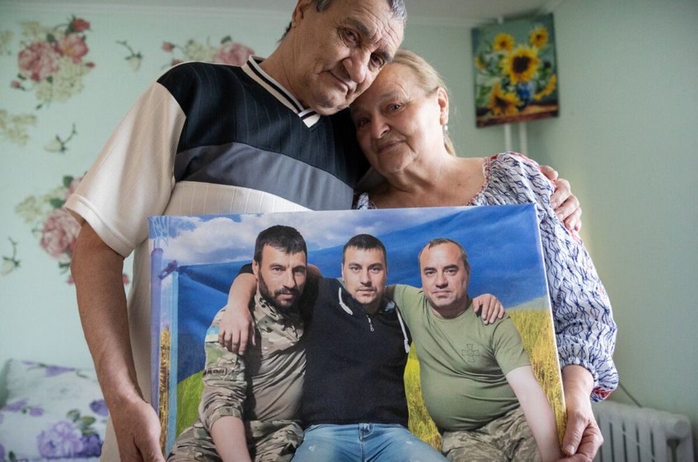 Mariia y Anatolii abrazados sostienen un cuadro con una foto familiar
